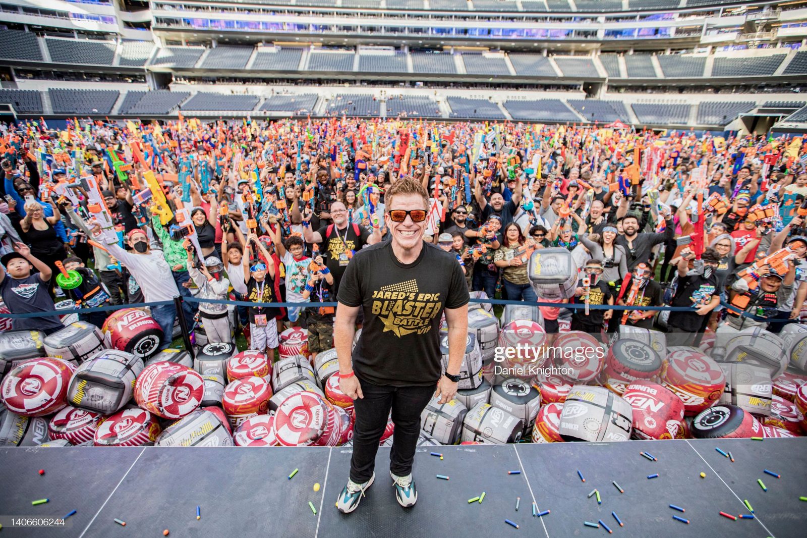 Jared Guynes standing on stage in front of a stadium full of players holding up their foam blasters