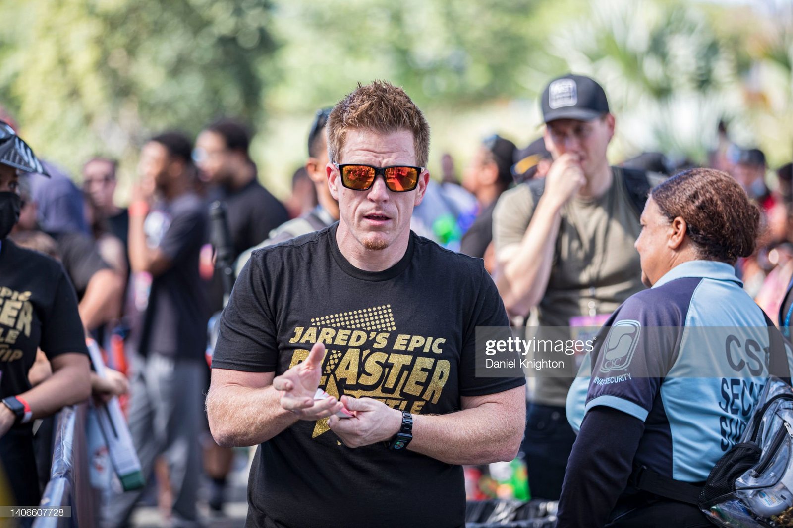 Jared Guynes in orange sunglasses and a Jared's Epic Blaster Battle shirt, talking with players in the crowd