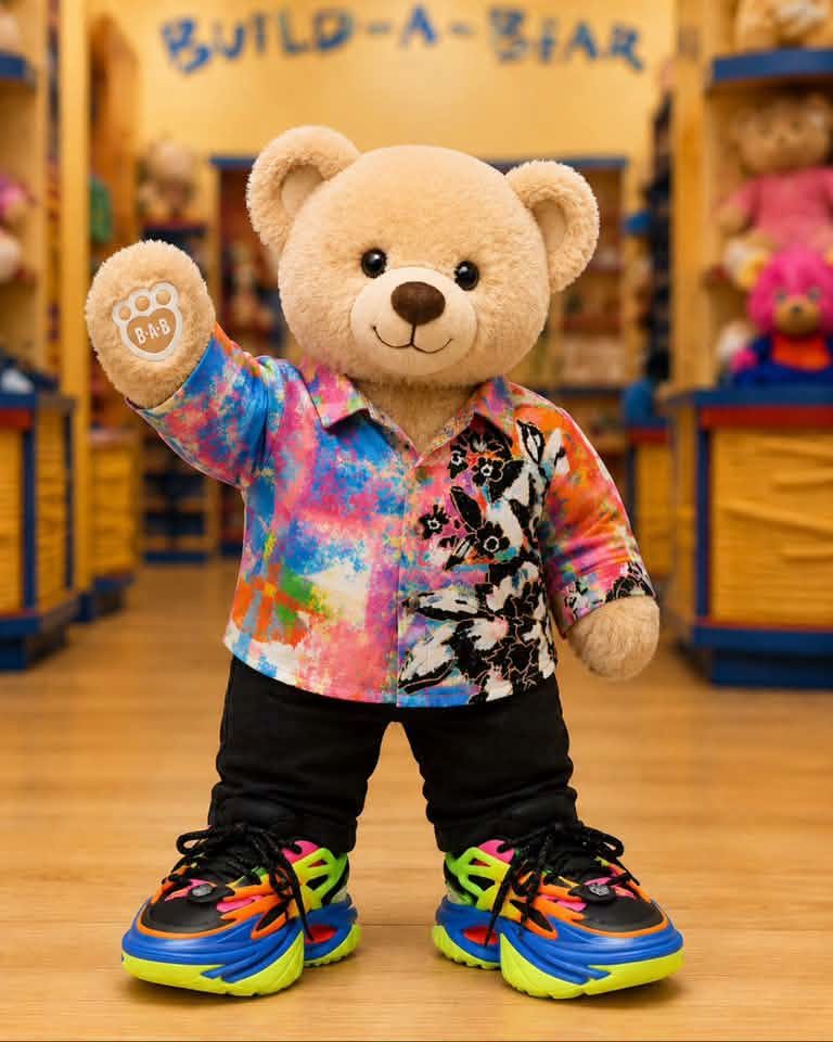 A Build-A-Bear teddy waving in a tiny copy of Jared's Floor outfit: the floral shirt, black jeans and rainbow trainers