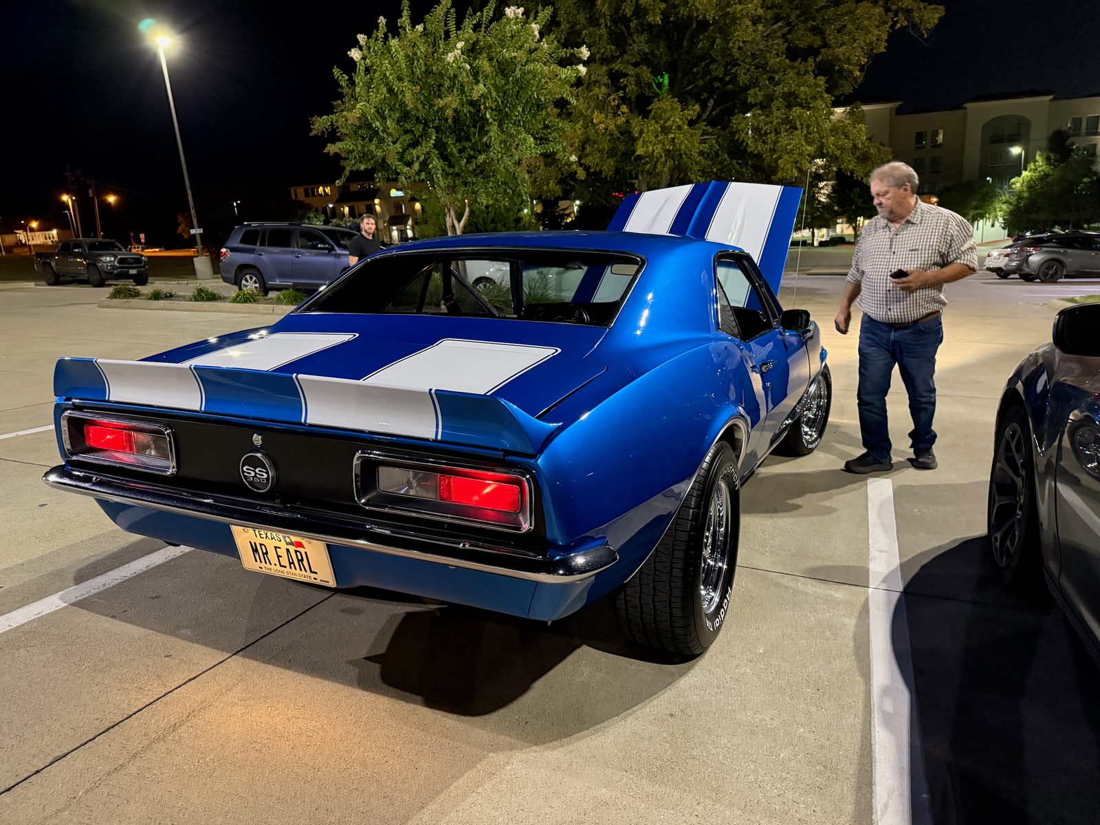 A man standing beside the restored 1967 Camaro with its MR EARL license plate at night