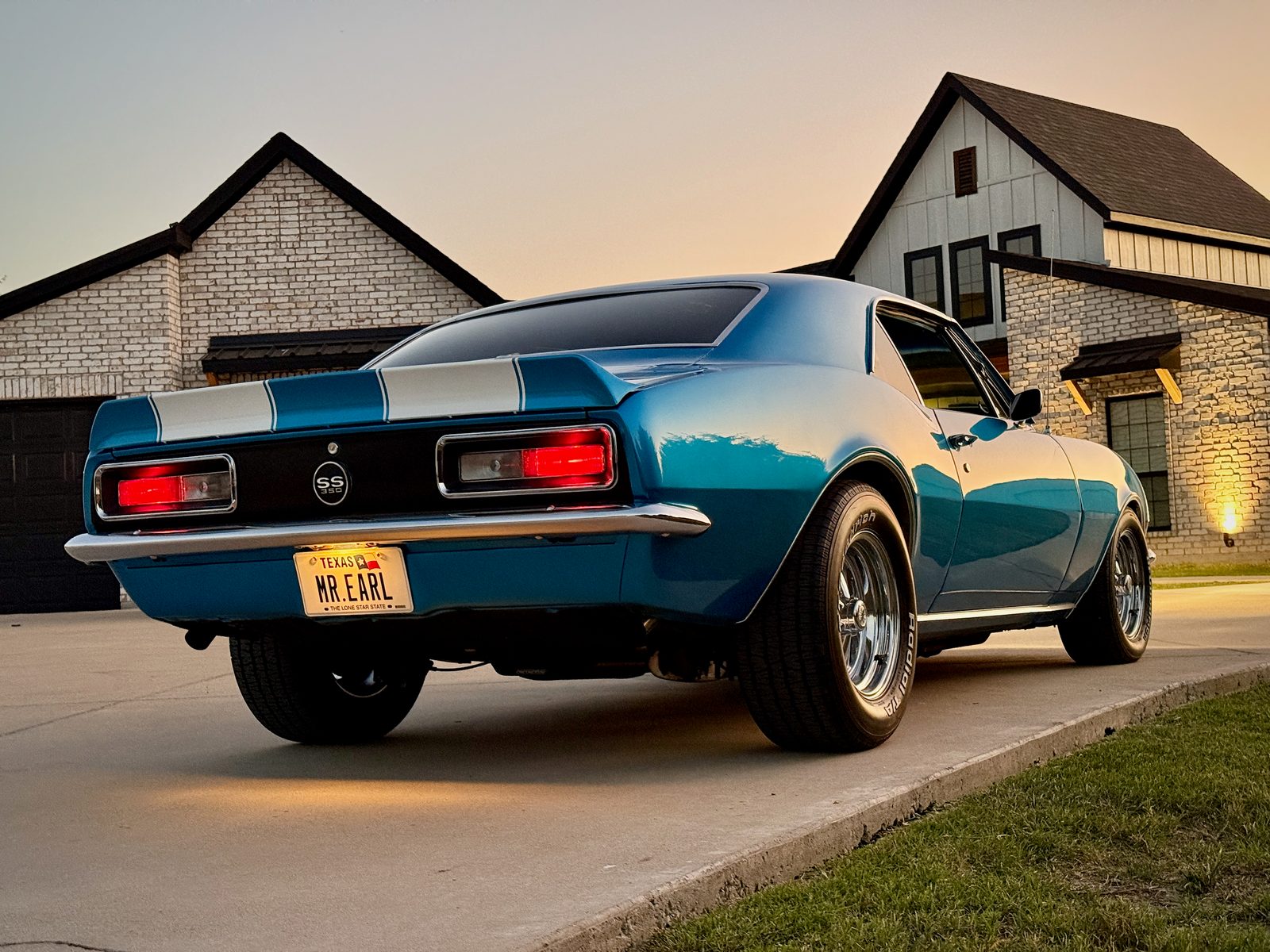 The back of the restored 1967 Camaro, with its MR EARL license plate, in a driveway at dusk