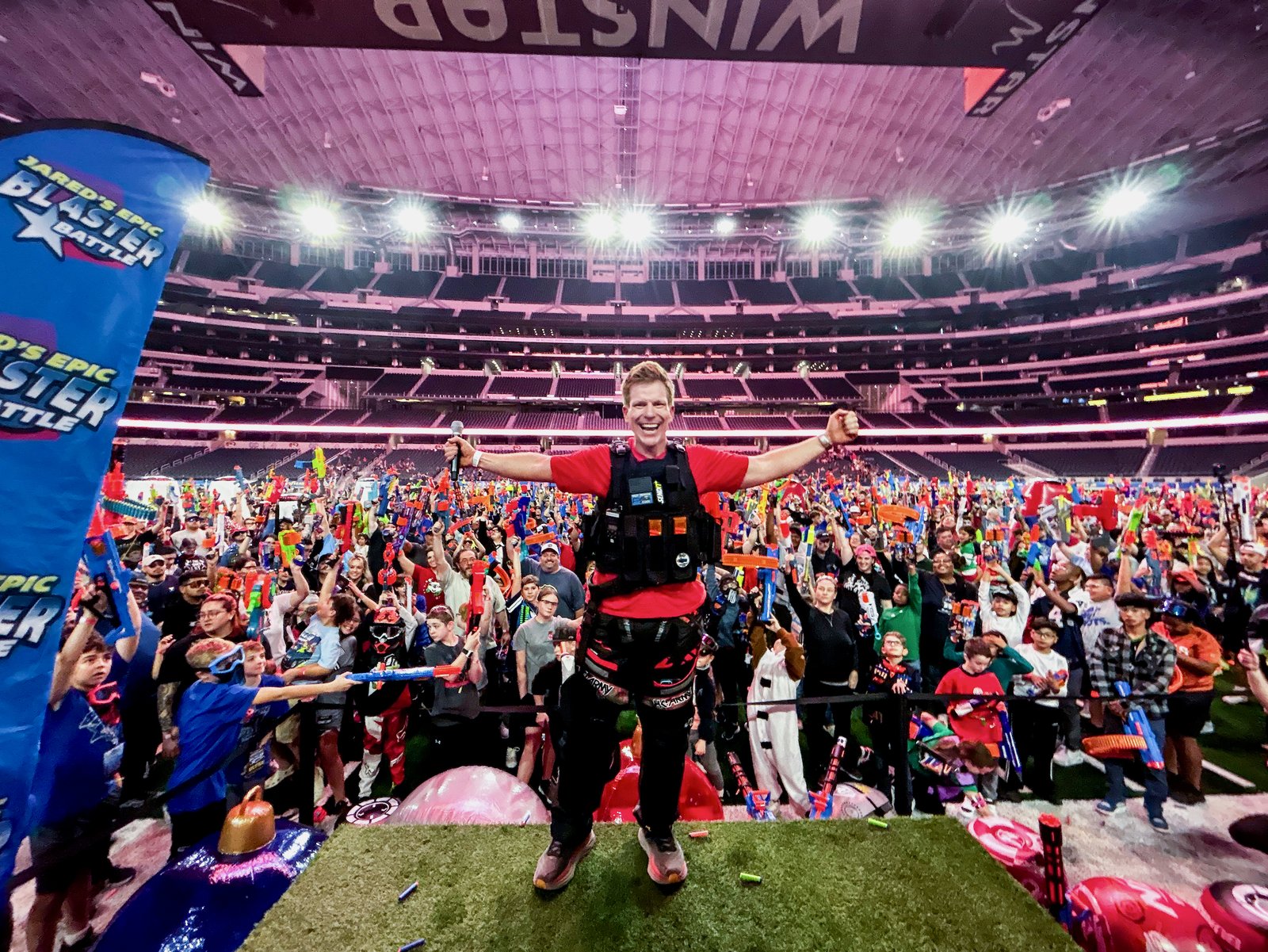 Jared Guynes on stage with his arms out at AT&T Stadium as a crowd of thousands raises their foam blasters