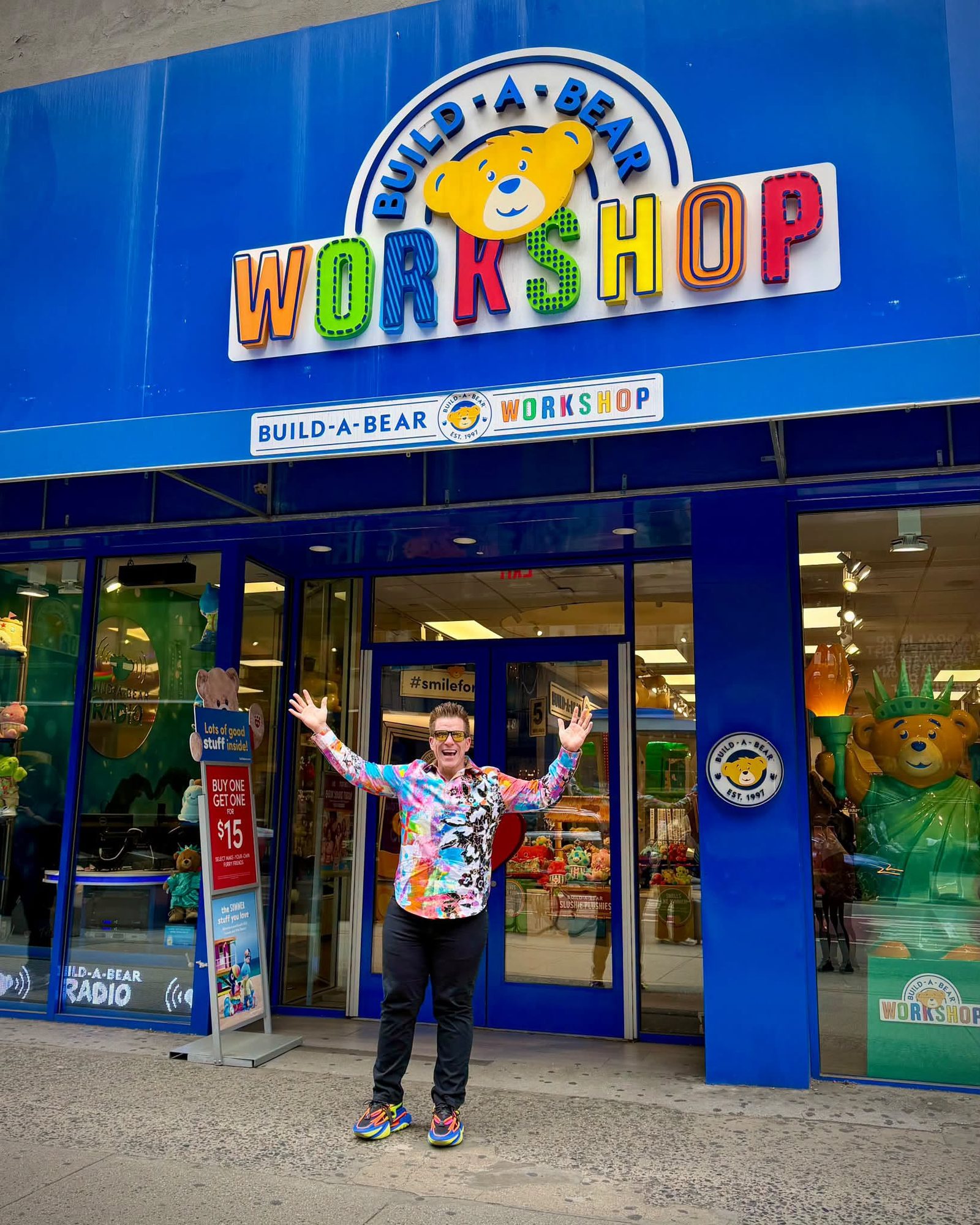 Jared Guynes throwing his arms up outside a Build-A-Bear Workshop, in his floral Floor shirt and rainbow trainers