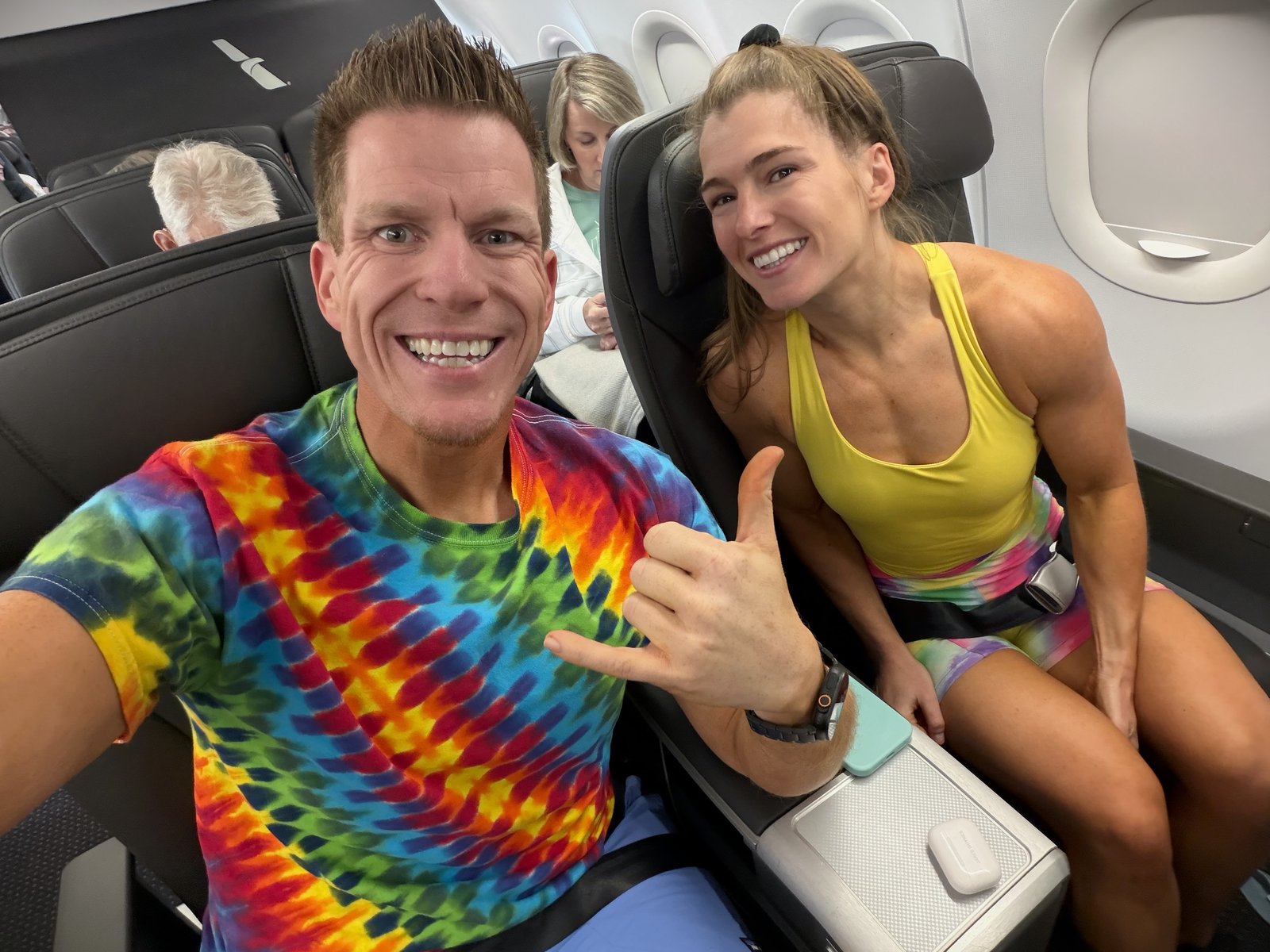 Jared Guynes in a tie-dye shirt on a flight, grinning at the camera