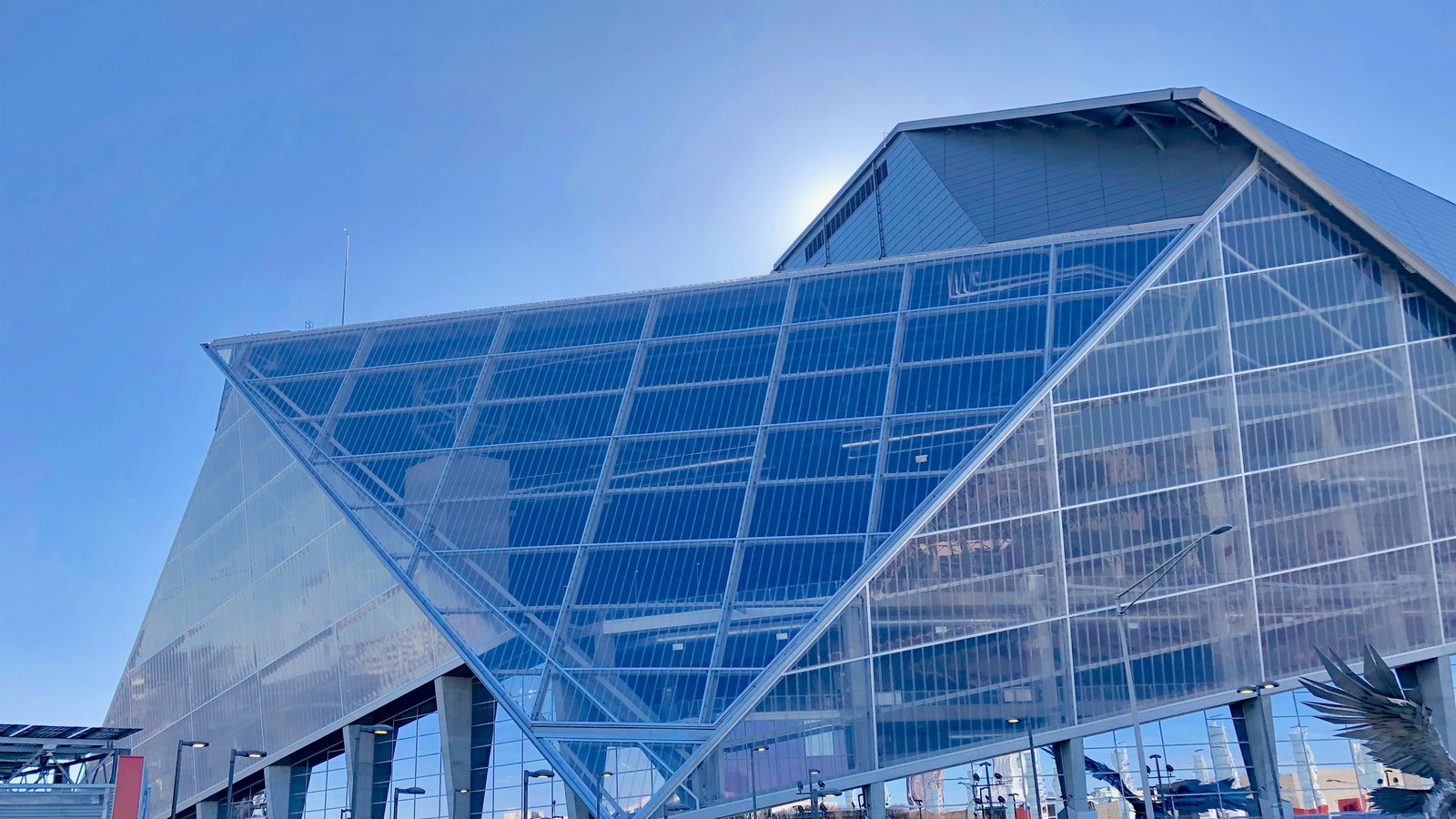The angled glass walls of Mercedes-Benz Stadium in Atlanta under a blue sky