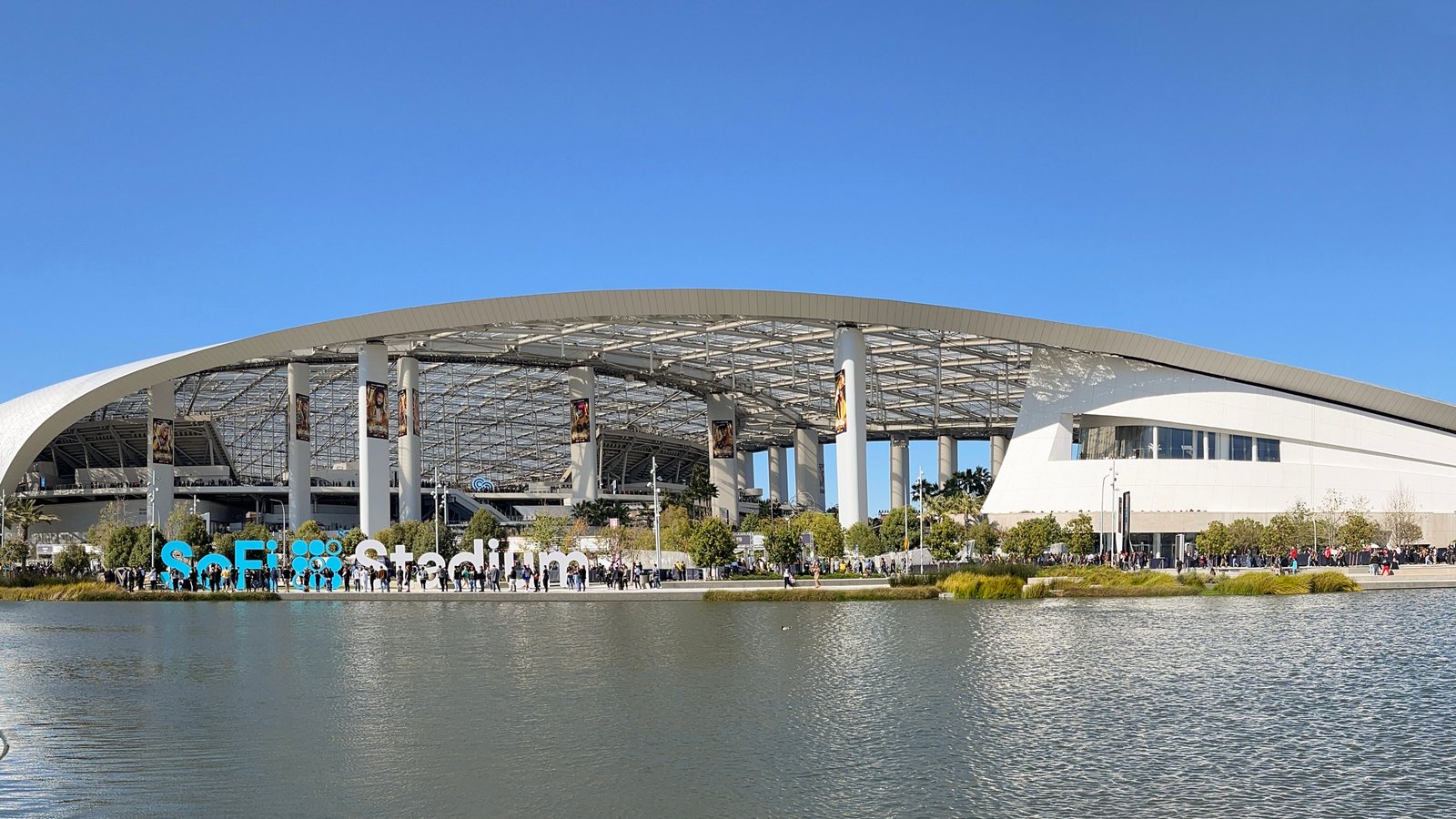 SoFi Stadium in Inglewood, California, seen across the lake under a clear blue sky